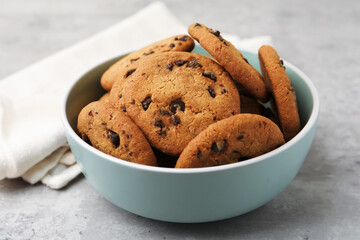 Delicious chocolate chip cookies in bowl on gray textured table, closeup