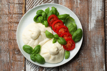 Delicious burrata cheese with basil and tomatoes on wooden table, top view