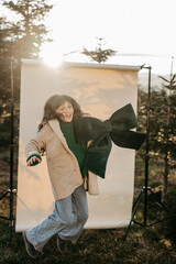 M&auml;dchen mit gr&uuml;ner Masche in der Hand steht vor beigem Studiohintergrund in der Natur