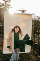 M&auml;dchen mit gr&uuml;ner Masche in der Hand steht vor beigem Studiohintergrund in der Natur