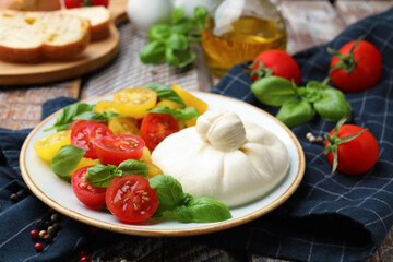 Delicious burrata cheese with basil and tomatoes on wooden table, closeup