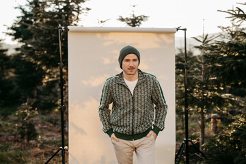 Mann in gr&uuml;ner Weste vor beigem Studiohintergrund in freier Natur