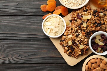 Tasty granola bars with dried fruits and nuts on black wooden table, flat lay. Space for text