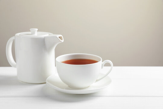 Hot tea in cup and teapot on white wooden table. Space for text