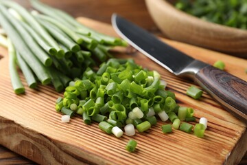 Cut green onions and knife on wooden table, closeup