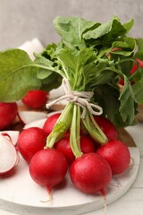 Fresh whole and cut radishes on white table against grey wall, closeup