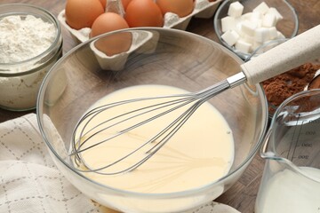 Different ingredients for dough and whisk on wooden table, closeup