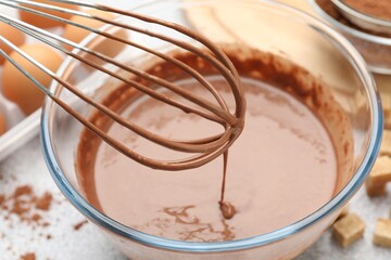 Dripping chocolate dough from whisk into bowl at grey table, closeup