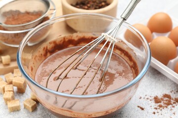 Chocolate dough with whisk in bowl and ingredients on grey textured table, closeup