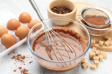 Chocolate dough with whisk in bowl and ingredients on grey textured table, closeup