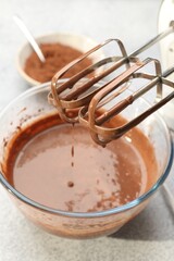 Dripping chocolate dough from mixer into bowl at grey textured table, closeup