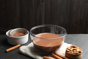 Liquid chocolate dough in glass bowl, cocoa powder, nuts and cinnamon on black table, closeup