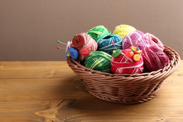 Many bright yarns with pins and buttons in wicker basket on wooden table against grey background, closeup. Space for text