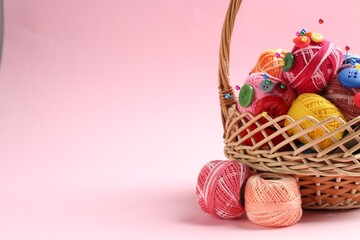 Bright yarns, pins, buttons and wicker basket on pink background, closeup. Space for text