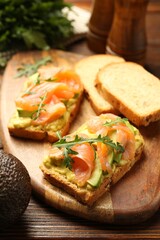 Tasty bruschettas with salmon, arugula and avocado on wooden table, closeup