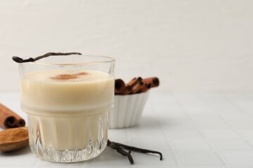 Delicious protein shake in glass, cinnamon and vanilla pods on white tiled table, closeup. Space for text