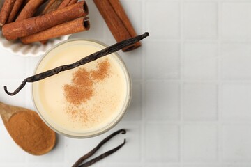 Delicious protein shake in glass, cinnamon and vanilla pods on white tiled table, flat lay. Space for text