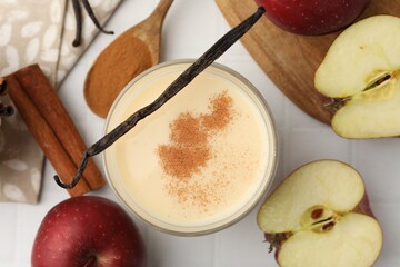 Delicious protein shake in glass, apples, cinnamon and vanilla pods on white tiled table, flat lay