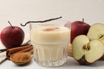 Delicious protein shake in glass, apples, cinnamon and vanilla pods on white table, closeup