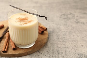 Delicious protein shake in glass, cinnamon and vanilla pods on grey table, closeup. Space for text