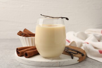 Delicious protein shake in glass, cinnamon and vanilla pods on grey table, closeup