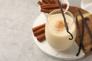 Delicious protein shake in glass, cinnamon and vanilla pods on grey table, closeup. Space for text