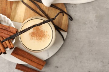 Delicious protein shake in glass, cinnamon and vanilla pods on grey table, top view. Space for text