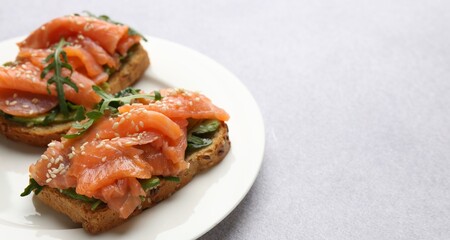 Tasty bruschettas with salmon, arugula and avocado on light grey table, closeup. Space for text