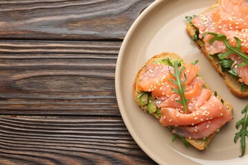 Tasty bruschetta with salmon, avocado, arugula and sesame seeds on wooden table, top view. Space for text