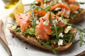 Tasty bruschetta with salmon, avocado, arugula, seeds and feta cheese on table, closeup