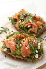 Tasty bruschetta with salmon, avocado, arugula, seeds and feta cheese on table, closeup