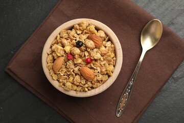 Tasty granola with dried fruits and nuts in bowl on black table, flat lay