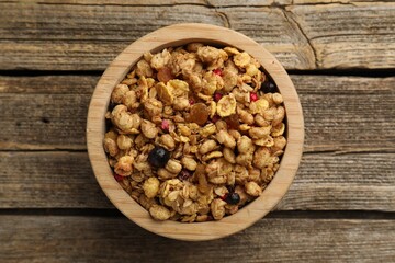 Tasty granola with dried fruits in bowl on wooden table, top view
