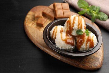 Tasty ice cream with caramel sauce and mint in bowl on black table
