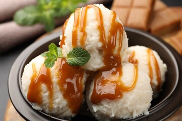 Tasty ice cream with caramel sauce and mint in bowl on table, closeup