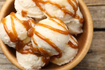 Tasty ice cream with caramel sauce in bowl on wooden table, top view
