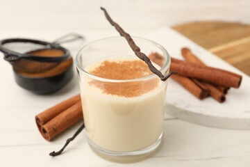 Delicious protein shake in glass, cinnamon and vanilla pods on white wooden table, closeup