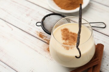 Delicious protein shake in glass, cinnamon and vanilla pod on white wooden table, closeup. Space for text