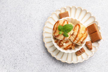 Tasty ice cream with caramel sauce, almonds and mint on light table, top view. Space for text