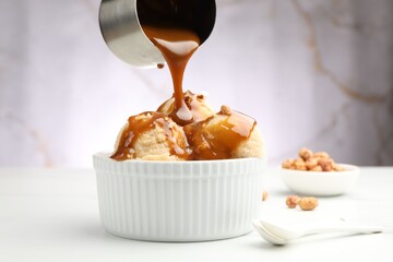 Pouring caramel sauce onto tasty ice cream with almonds at white table, closeup