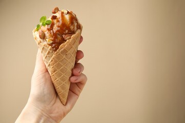 Woman holding ice cream with caramel sauce, almonds and mint on beige background, closeup. Space for text