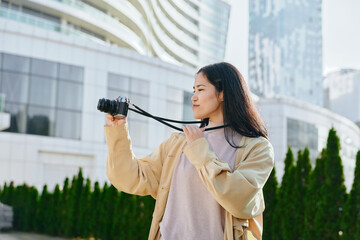 Woman with camera in hand capturing urban scenery in an outdoor setting with modern buildings,...