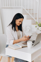 Online instructor updates learning resources, Smiling woman utilizing laptop in cheerful home environment, Female freelancer joyfully engaged in typing and communicating from cozy home workspace