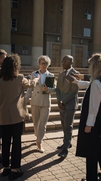 Full vertical shot of Caucasian female barrister, carrying briefcase, walking out of court hall, protected by African American bodyguard, refusing to provide comments on lawsuit to media reporters