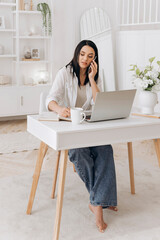 Freelancer woman managing tasks efficiently, Calm freelancer woman multitasking with laptop and phone nearby, Relaxed woman professional multitasking at cozy white desk with coffee and decor
