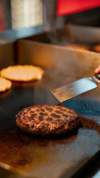 Grilled beef burger patty on hot flat top griddle, metal spatula pressing seared meat, steam rising from cooking surface, juicy fast food preparation, street food cooking scene