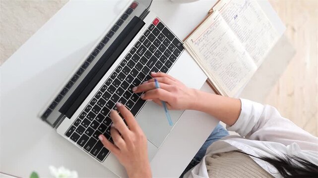 Focused woman typing on laptop, Caucasian woman meticulously editing documents on computer, Caucasian woman engaging in detailed editing while referencing handwritten notes and digital documents