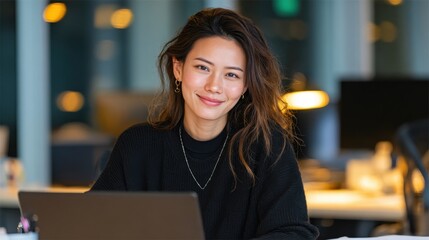 Asian business woman works on laptop at desk in modern office during daytime hours engaging in tasks related to her profession