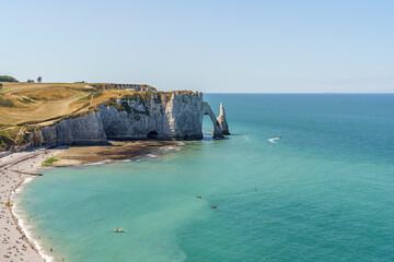 Sarkozy Beach and Rocky Coast, made of stone, extending into the blue water of the ocean in the city of Etretat France The sky is blue The stone arch resembles an elephant's nose