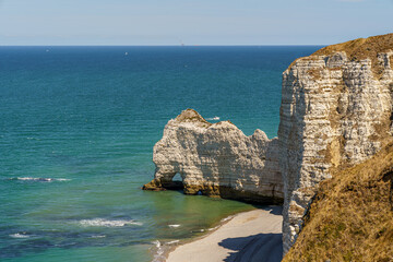 A cliff in the ocean with a rock resembling an elephant in the Etretat, Normandy, France The beach is visible below. And the calm blue water The water is blue, the sky is calm and transparent
